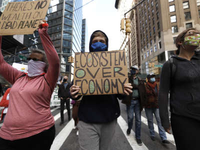 A masked protester holds a sign reading "ECOSYSTEM OVER ECONOMY" during a protest