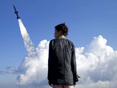 A woman stands in the foreground as a missile is launched into the sky