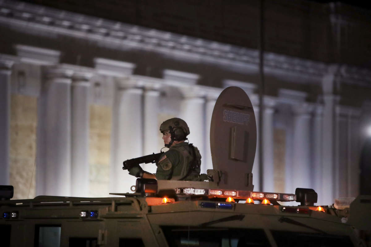 A soldier stands up through the sunroof of an armored vehicle