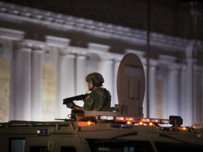 A soldier stands up through the sunroof of an armored vehicle