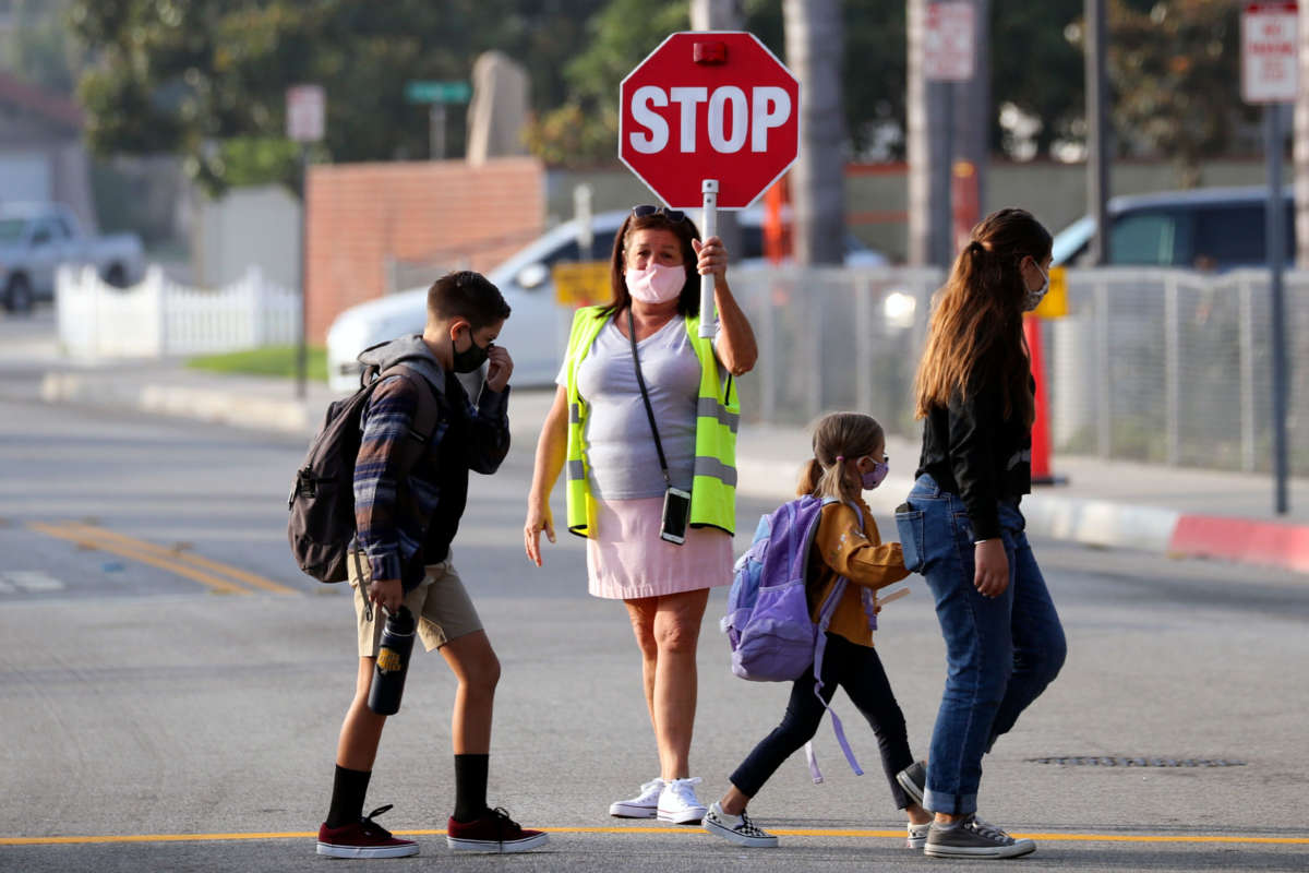 A crossing guard help cross the street as students return, after months of closure due COVID-19 pandemic, at James H. Cox Elementary School on September 23, 2020 in Fountain Valley, California.