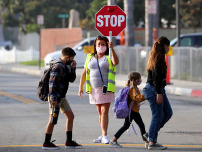 A crossing guard help cross the street as students return, after months of closure due COVID-19 pandemic, at James H. Cox Elementary School on September 23, 2020 in Fountain Valley, California.