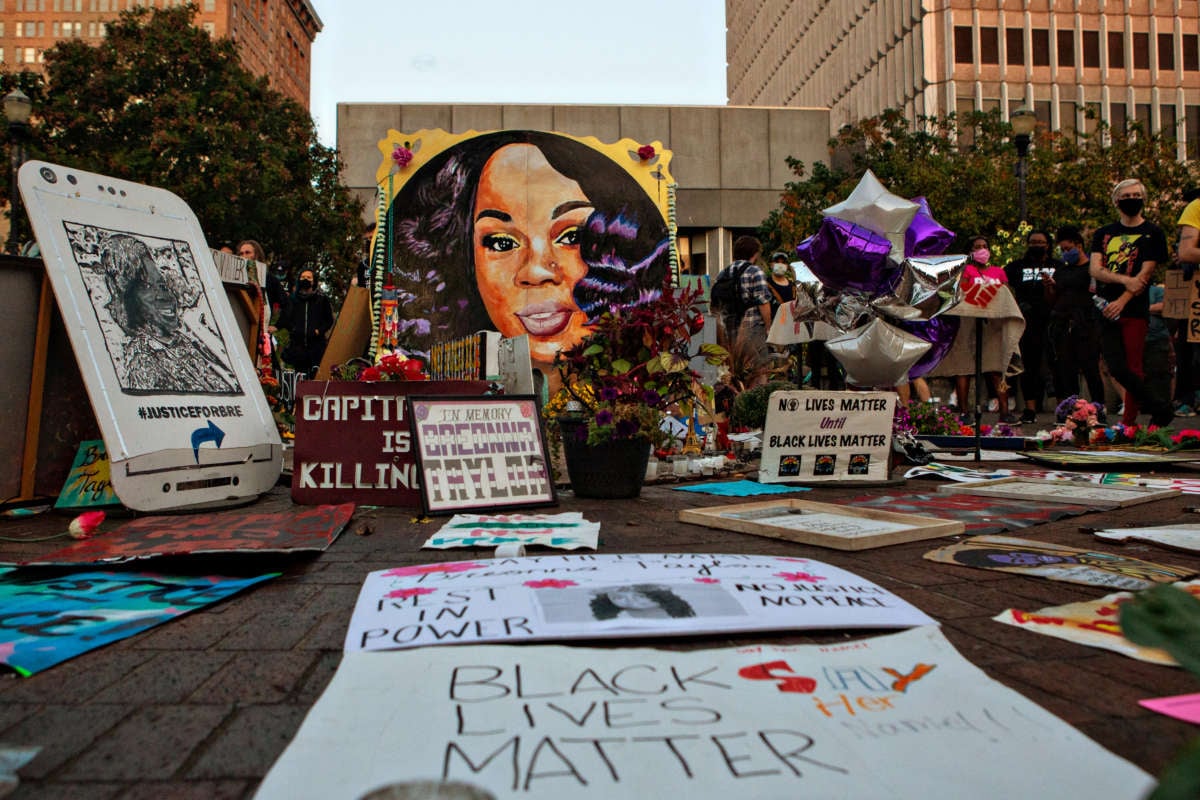 Flowers and protest signs are displayed around a mural of Breonna Taylor
