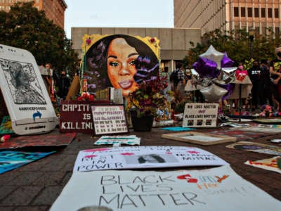 Flowers and protest signs are displayed around a mural of Breonna Taylor