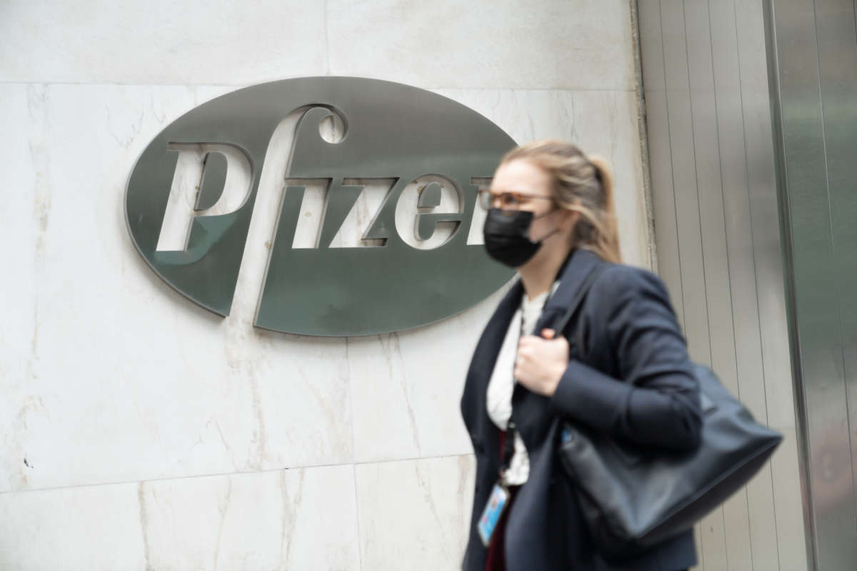 A woman wearing a face mask walks past a Pfizer logo at their Headquarters. Pfizer's coronavirus vaccine could be given to Americans before end of the year, the CEO says.