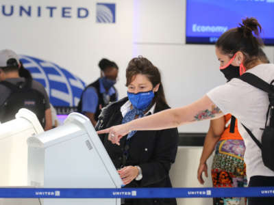 A United Airlines employee wears a required face covering along with a passenger at check-in at Los Angeles International Airport on October 1, 2020, in Los Angeles, California. United Airlines and American Airlines are set to start furloughing 32,000 employees after negotiations for a new coronavirus aid package failed in Washington.