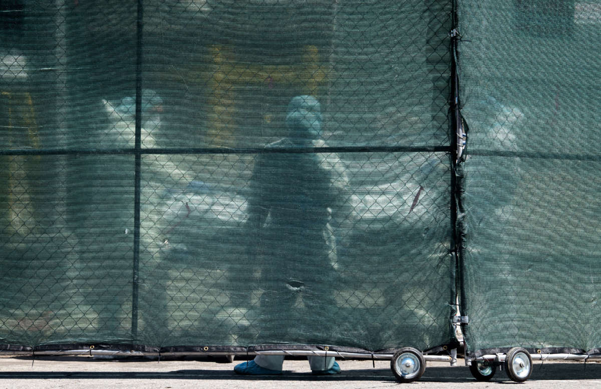 Hospital personnel behind a barricade move deceased individuals to the overflow morgue trailer outside The Brooklyn Hospital Center on May 7, 2020, in the Brooklyn borough of New York City.