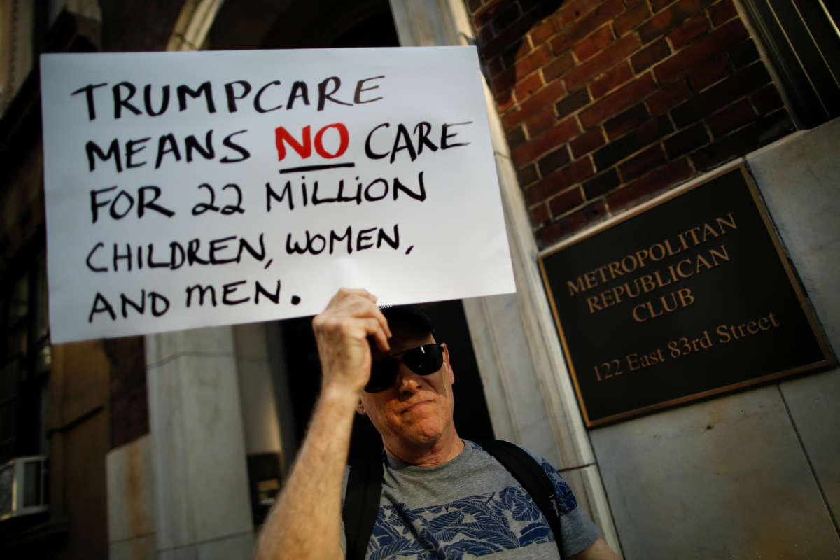 A protester holds a sign reading "TRUMPCARE MEANS NO CARE FOR 22 MILLION CHILDREN, WOMEN AND MEN" during a pre-covid protest