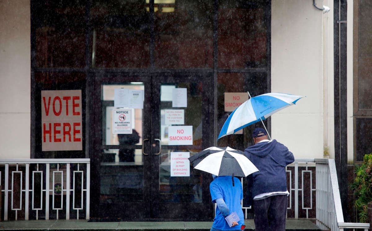 Two people walk under umbrellas outside a polling station at Dallas County Courthouse during the presidential primary in Selma, Alabama, on Super Tuesday, March 3, 2020.