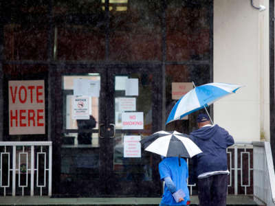 Two people walk under umbrellas outside a polling station at Dallas County Courthouse during the presidential primary in Selma, Alabama, on Super Tuesday, March 3, 2020.