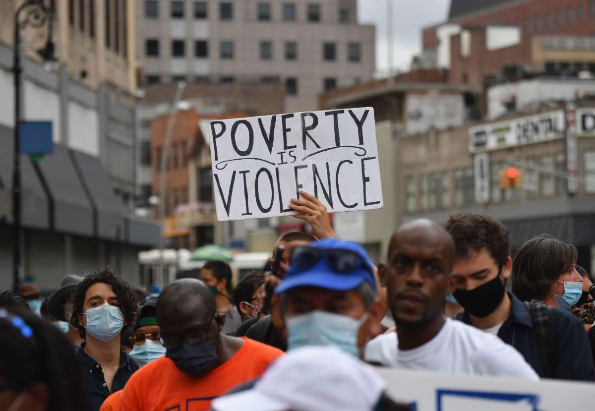 A protester holds a sign reading "POVERTY IS VIOLENCE" during an outdoor rally