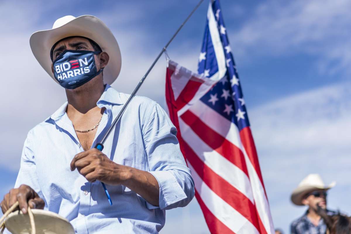 A man in a Biden/Harris mask gazes handsomely forward while holding a u.s. flag