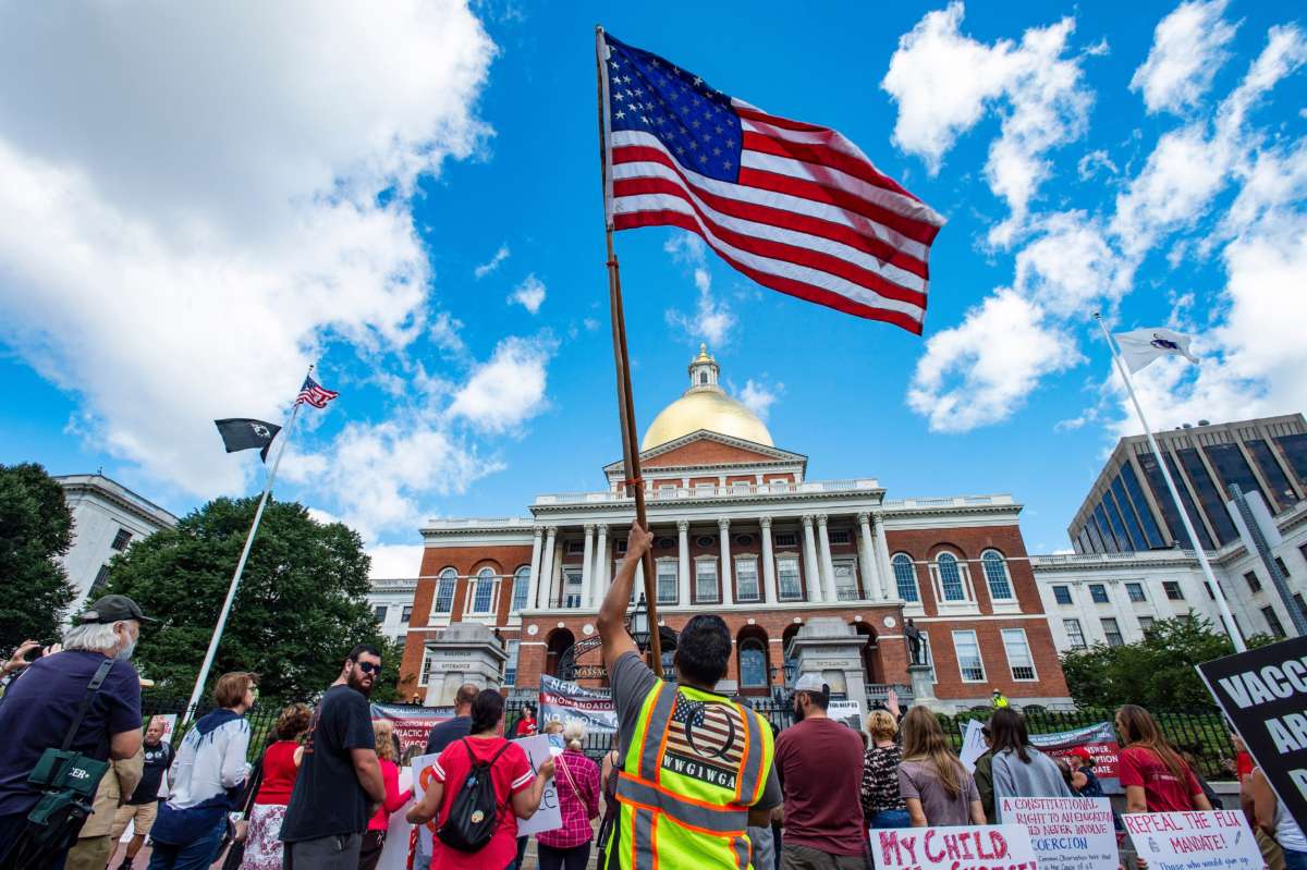 A man with a QAnon vest and US Flag joins hundreds of people protesting a mandate from the Massachusetts Governor requiring all children in grades K-12 to receive an influenza (flu) vaccine/shot to attend school for the 2020/2021 year outside the Massachusetts State House in Boston on August 30, 2020.