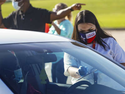 An election worker accepts mail-in ballot from a voter at drive-thru mail ballot drop-off site at NRG Stadium on October 7, 2020, in Houston, Texas.