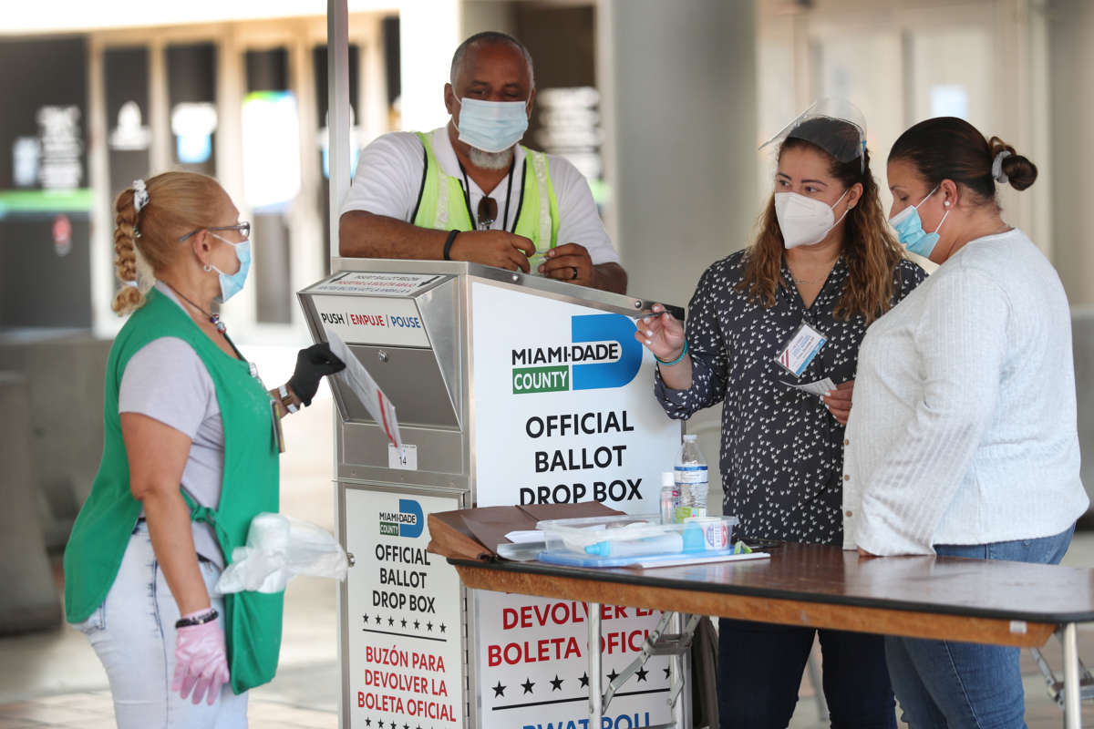 Poll workers help a voter put their mail-in ballot in an official Miami-Dade County ballot drop box on August 11, 2020, in Miami, Florida.