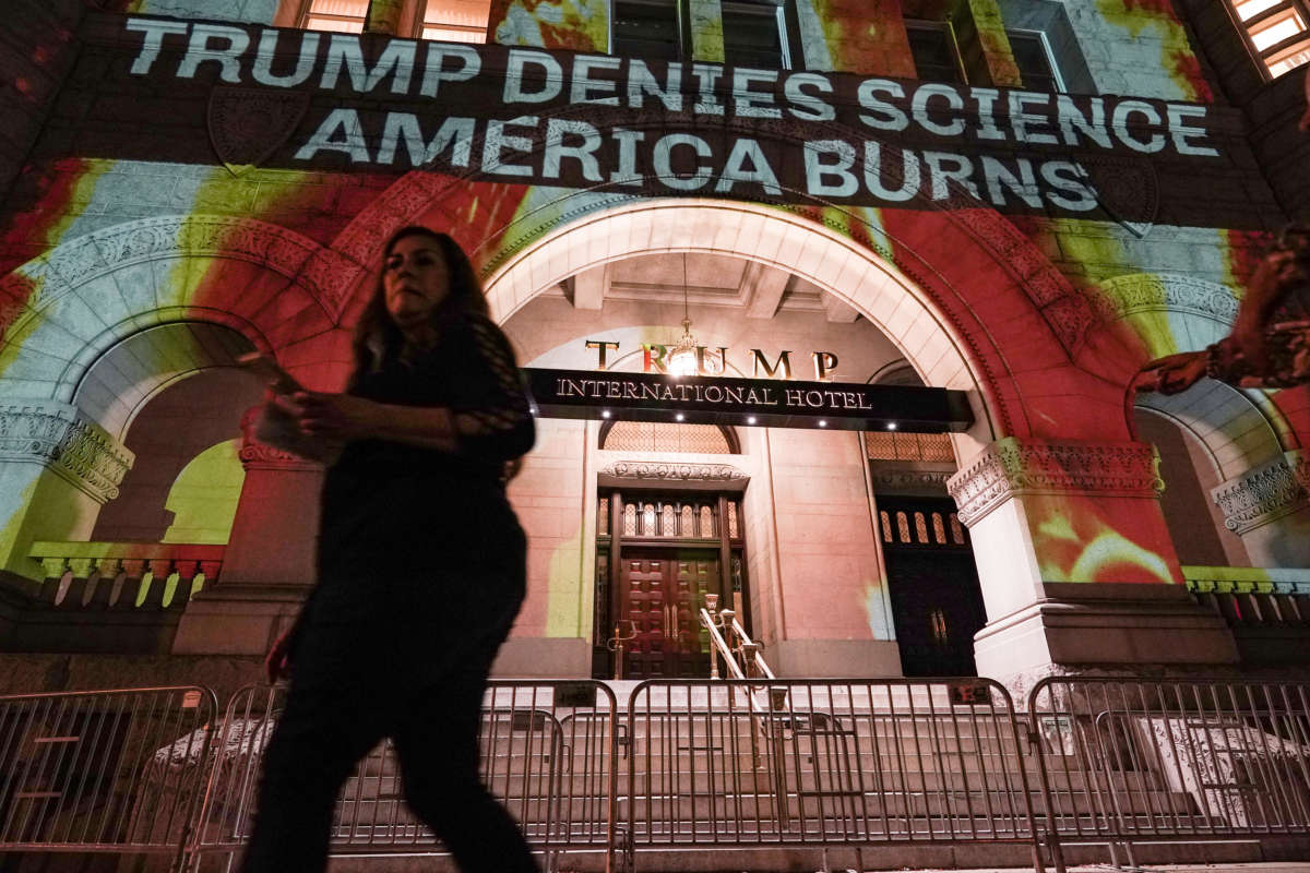 A woman walks by a projection of flames and commentary on the side of the Trump International Hotel organized by activists in protest of President Donald Trump's response to science and climate change in the face of devastating wild fires burning throughout the United States on October 21, 2020, in Washington, D.C.