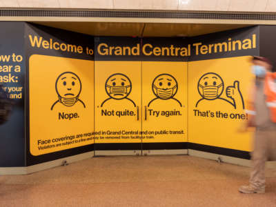 People wearing a mask walk past an instructional mask sign in Grand Central Terminal on October 23, 2020, in New York City.