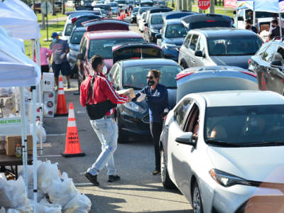 Volunteers help load food as vehicles arrive to pick up food supplies and essential items during a Feeding South Florida Drive-Thru Food Distribution at Miramar Regional Park on November 19, 2020, in Miramar, Florida.