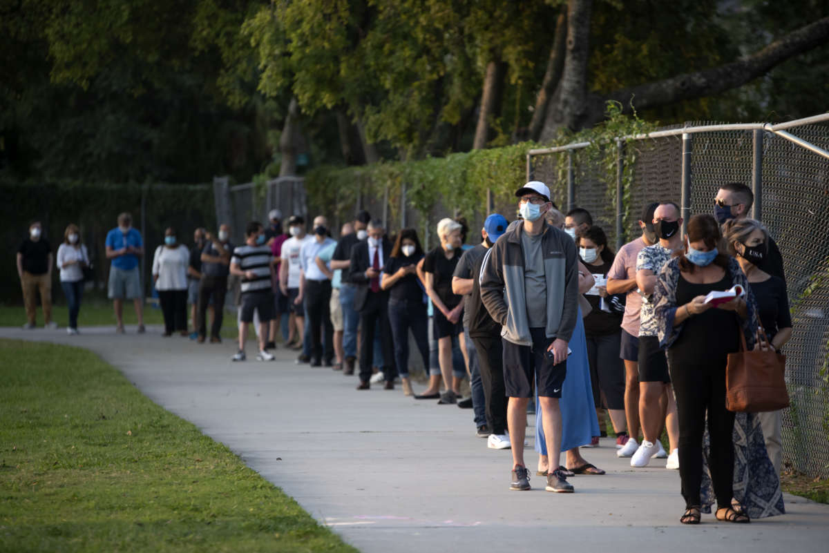 a line of voters waits beside a chainlink fence to vote