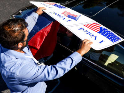 A poll worker shields the voting screen as a man votes from his car during curbside voting at Seacoast Church West Ashley on October 30, 2020, in Charleston, South Carolina.