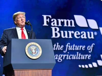 Donald Trump speaks in front of a blue backdrop reading "Farm Bureau"