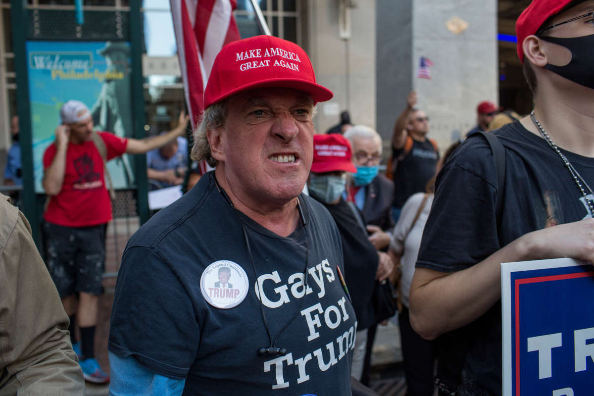A man in a trump hat makes the facial equivalent of a growl during a small rally
