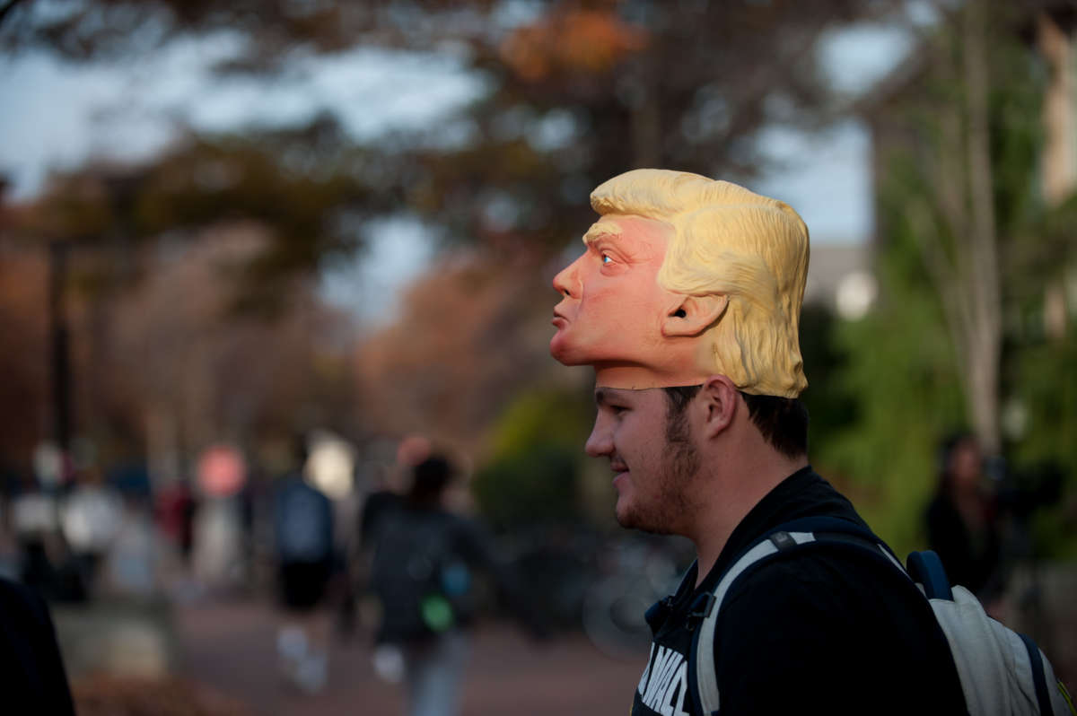 A college-aged young man wears a Trump mask like a hat