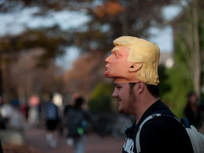 A college-aged young man wears a Trump mask like a hat