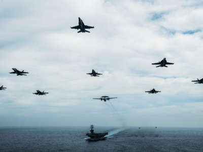 Aircraft fly in formation over the USS Nimitz in the Pacific Ocean, June 2, 2020, while the aircraft carrier is underway for a composite training unit exercise.