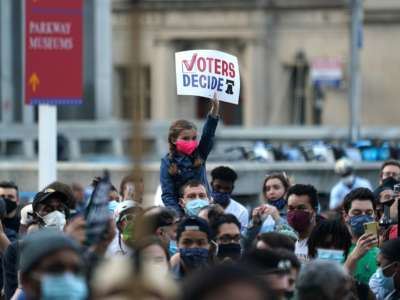A girl holds a sign reading "VOTERS DECIDE" while sitting on her dad's shoulders during a protest