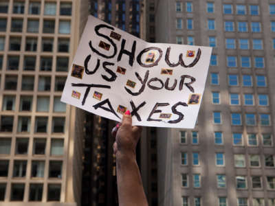 A protester holds up a sign reading "SHOW US YOUR TAXES"