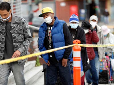 Masked people wait in a line for food