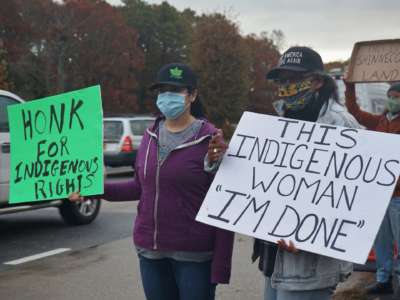 Masked Indigenous activists display signs during a roadside protest