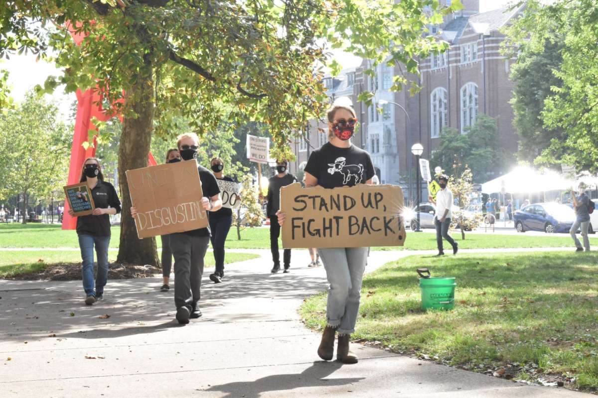 Masked activists march with handwritten signs, the closest one reading "STAND UP, FIGHT BACK"