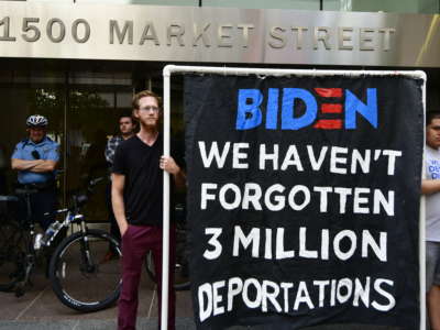 Two activists display a banner reading "BIDEN: WE HAVEN'T FORGOTTEN 3 MILLION DEPORTATIONS"