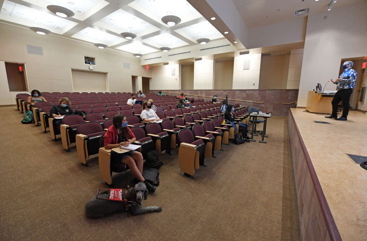 College students sit in a sparsely populated auditorium classroom to learn