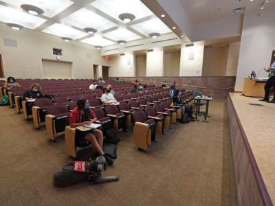 College students sit in a sparsely populated auditorium classroom to learn