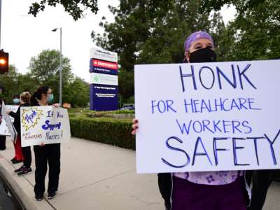 A masked nurse holds a sign reading "HONK IF YOU SUPPORT NURSES" during a curbside covid-era protest