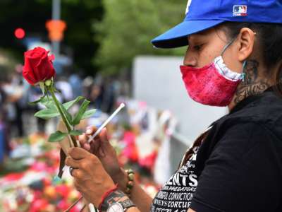 A masked woman holds a rose near a memorial