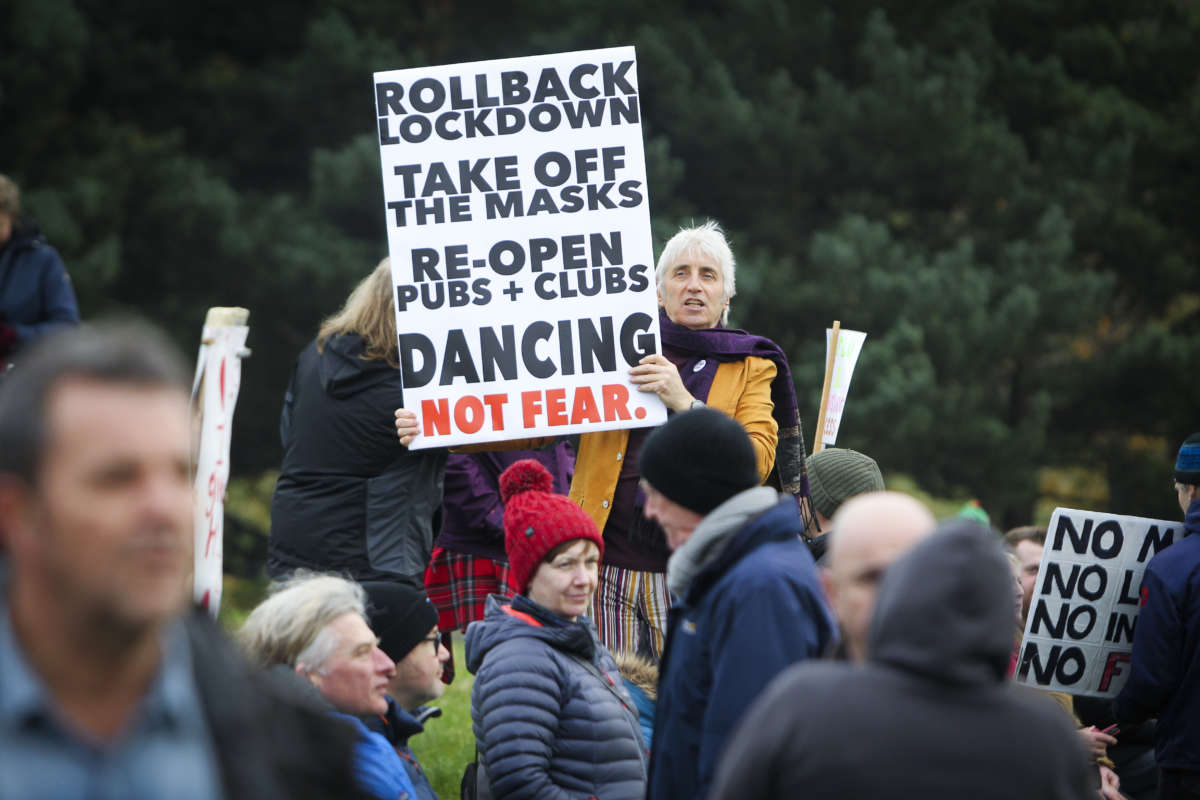 An unmasked protester holds a sign reading "ROLLBACK LOCKDOWN, TAKE OFF THE MASKS, RE-OPEN PUBS + CLUBS, DANCING NOT FEAR." during a protest