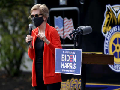 A masked Elizabeth Warrenspeaks while standing on a podium