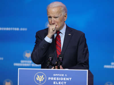 An unmasked President Elect Joseph R. Biden coughs into his hand in the age of covid