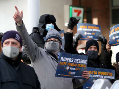 Members of the crowd hold signs reading MBTA riders deserve safe public transit and cheer during a rally