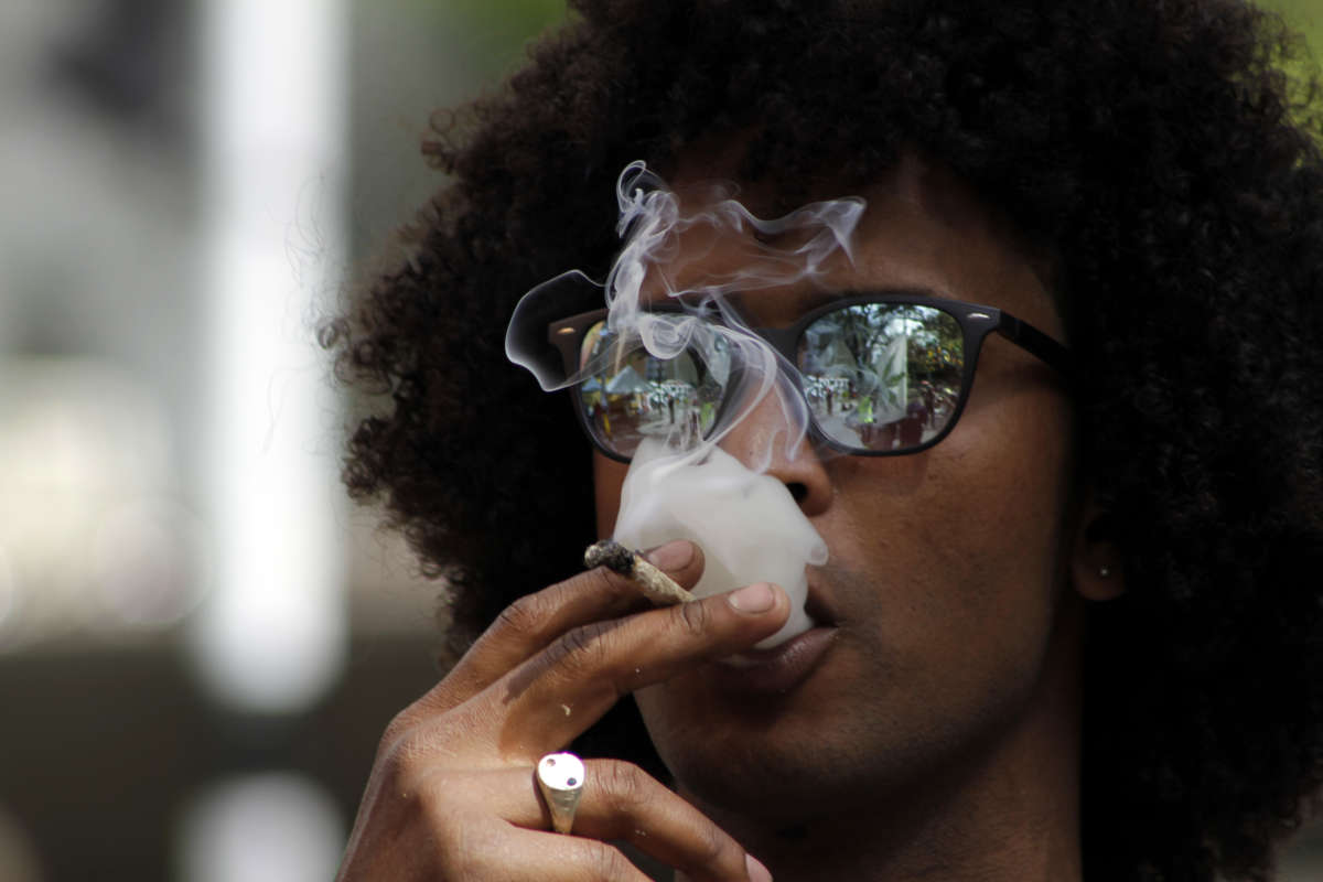 A young man in reflective sunglasses smokes a joint