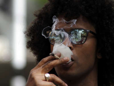 A young man in reflective sunglasses smokes a joint