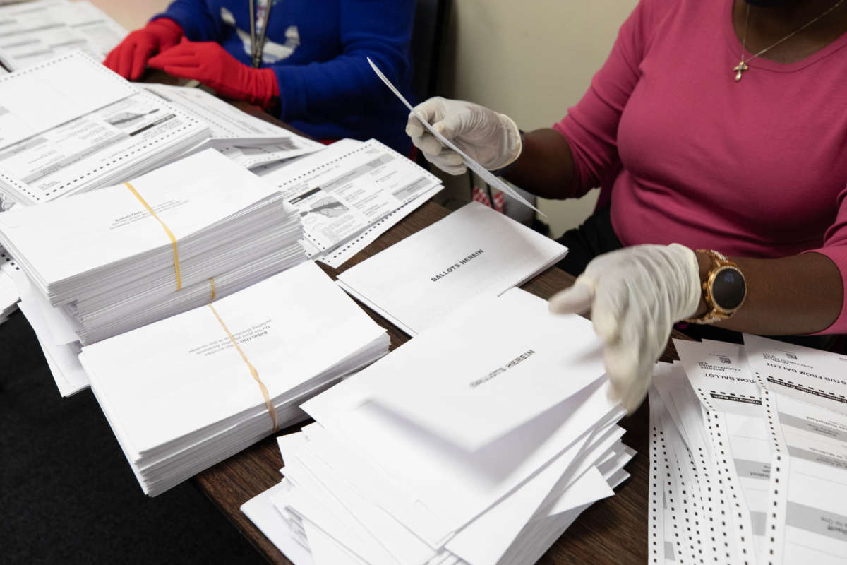 A ballot counter handles a piles upon piles of paper ballots