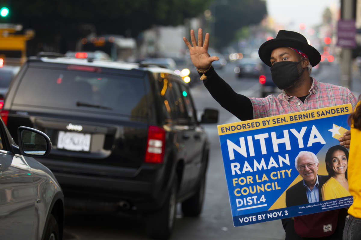 As the sun begins to set, Matthew Gaston of Los Angeles holds up a vote sign for Nithya Raman for LA City Council down the street from a voting center inside The Wiltern on election day on November 3, 2020, in Los Angeles, CA.