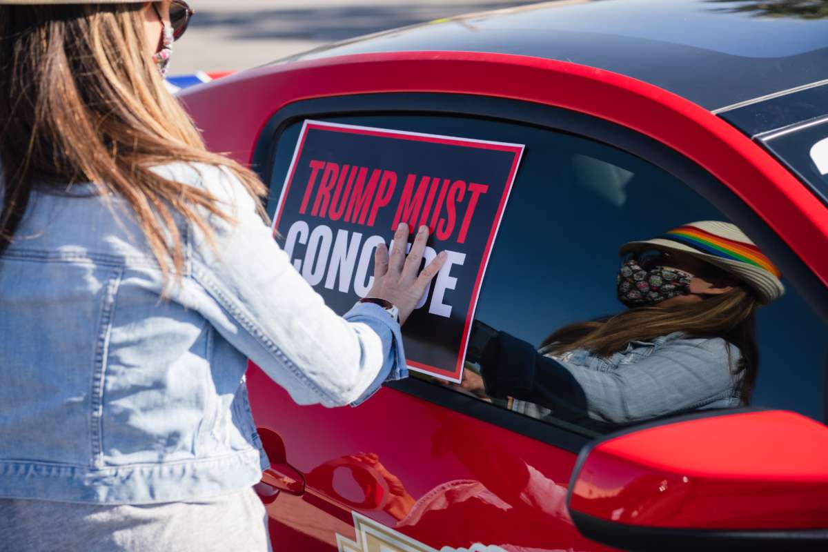 A woman tapes a "TRUMP MUST CONCEDE" sign to the side of her car