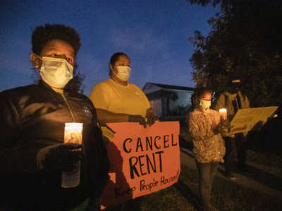 Masked people hold signs during a candlelight vigil decrying evictions