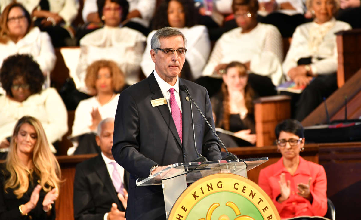 The real Brad Raffensperger speaks at a podium in a church